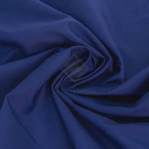 May include: A solid deep blue fabric with a smooth, matte texture. The material is gathered in the centre, creating soft, flowing folds and shadows that highlight the consistent, rich navy colour throughout the entire surface of the textile.
