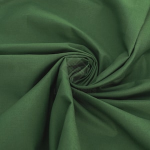 Puede incluir: Una tela de color verde bosque oscuro sólido con una textura suave y mate. El material está recogido en el centro, creando pliegues suaves y fluidos y sombras profundas que irradian hacia afuera, resaltando el color uniforme del tejido.