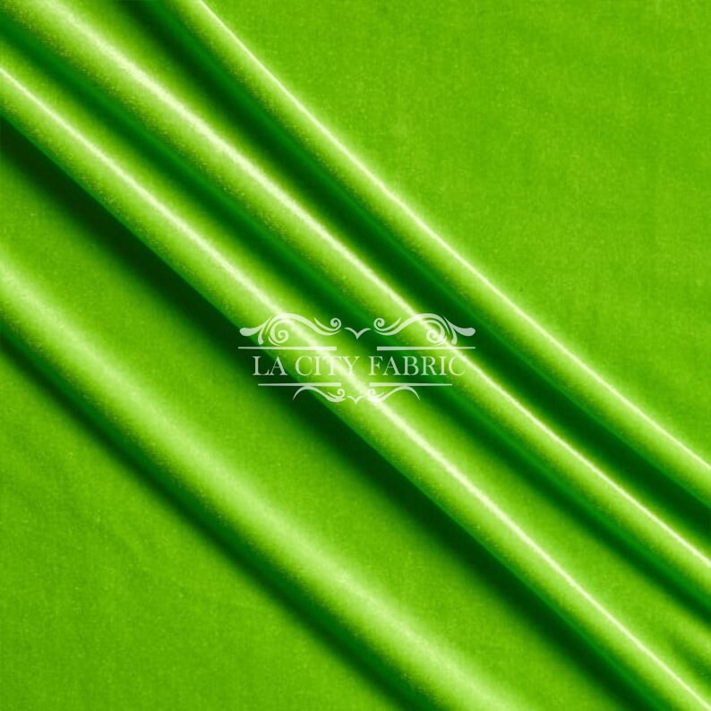 May include: A bright green velvet fabric with a subtle sheen. The fabric is folded in a diagonal pattern, creating a smooth, flowing texture. The fabric is labeled "LA City Fabric".