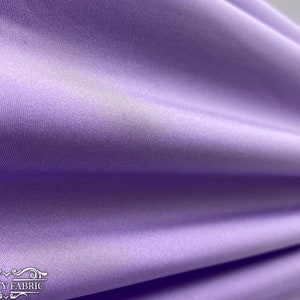 Puede incluir: Primer plano de una tela suave de color lila claro con un brillo sutil. La tela est&aacute; drapeada y doblada, mostrando su textura y ca&iacute;da.