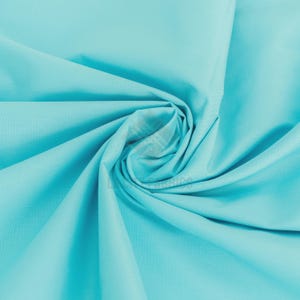 May include: A solid light turquoise fabric with a smooth texture, arranged in a central spiral fold that creates radiating pleats and soft shadows across the surface. The fabric features a subtle watermark logo reading LUCKY FABRICS.
