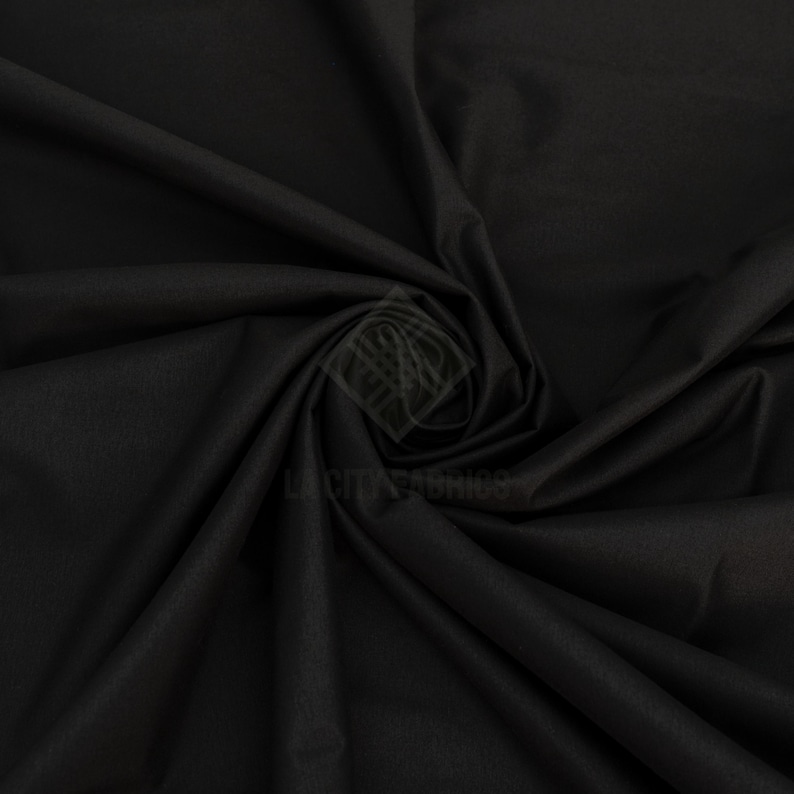 May include: A solid black fabric with a smooth, matte texture, arranged in a swirling, draped pattern. A faint, semi-transparent watermark logo featuring the text LA CITY FABRICS is visible in the center of the fabric folds.