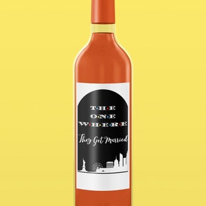 Op de afbeelding: Een wijnfleslabel met een zwart-wit ontwerp met de tekst "THE ONE WHERE They Get Married" in een gestileerd lettertype. Het label bevat ook een silhouet van de skyline van New York.