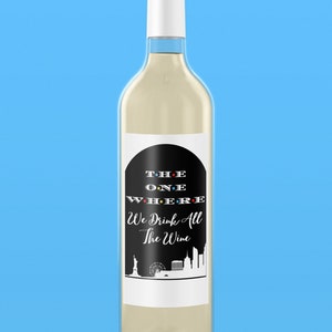 Op de afbeelding: Een witte wijnfles met een zwart-wit etiket waarop staat "The One Where We Drink All The Wine". Het etiket heeft een zwarte boog met de woorden "THE ONE WHERE" in wit met gekleurde stippen. Het etiket heeft ook een zwart-witte illustratie van de skyline van New York.
