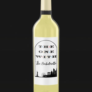 Op de afbeelding: Witte wijnfles met een etiket waarop "The One With The Bachelorette" staat in zwarte tekst met gekleurde stippen. Het etiket toont ook een zwart silhouet van de skyline van New York.