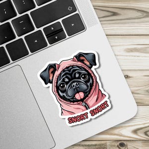 May include: A sticker featuring a black pug wearing a pink hoodie with the text "Snort Snort". The pug has a pink tongue sticking out. The sticker is on a laptop.