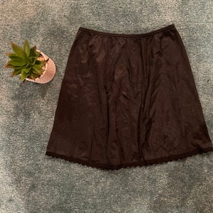 May include: A black slip skirt with a lace trim. The skirt is made of a silky material and has a gathered waist.