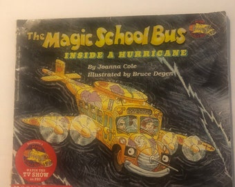 May include: The Magic School Bus book cover features a yellow school bus flying through a dark stormy sky with the text "The Magic School Bus Inside a Hurricane" and "By Joanna Cole Illustrated by Bruce Degen".