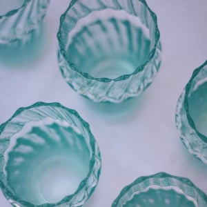 Op de afbeelding: Set van zes tealblauwe glazen bekers met een wit swirl-ontwerp. De bekers zijn perfect om drankjes te serveren of als decoratieve accenten.
