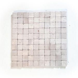 Könnte beinhalten: Eine quadratische Anordnung kleiner, hellfarbiger quadratischer Fliesen. Die Fliesen haben eine gedämpfte, cremefarbene Farbe mit subtilen Variationen, wodurch ein strukturiertes Aussehen entsteht. Die Fliesen sind gleichmäßig angeordnet und bilden ein Rastermuster, geeignet für die Inneneinrichtung.