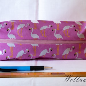 Könnte beinhalten: Rosa Reißverschluss-Tasche mit Flamingomuster. Die Tasche liegt auf einer weißen Oberfläche mit einem Lineal und einem Stift.