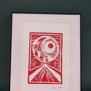 Puede incluir: Una impresión linograbada roja y blanca de un paisaje urbano con un gran sol rojo en el cielo. La impresión está enmarcada en un marco negro y firmada "Caron Peppe".