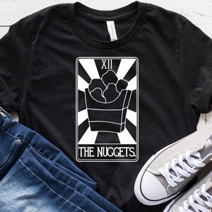 May include: Black t-shirt with a white graphic of a tarot card. The card is labeled "XII The Nuggets." The card depicts a box of chicken nuggets.