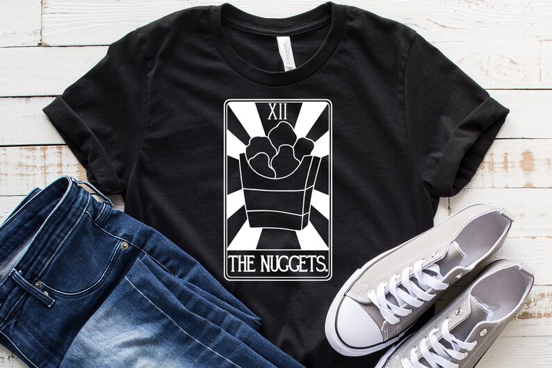 May include: Black t-shirt with a white graphic of a tarot card. The card is labeled "XII The Nuggets." The card depicts a box of chicken nuggets.