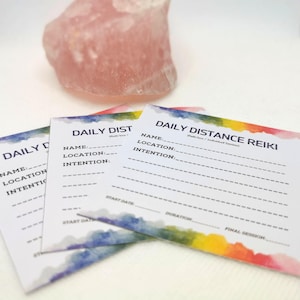 May include: Three white cards with a rainbow watercolor design. The cards are labeled "Daily Distance Reiki" and have lines for writing the name, location, and intention of the person receiving the Reiki session. The cards also have lines for writing the start date, duration, and final session.