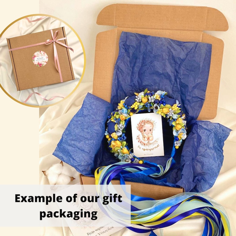May include: A blue and yellow floral crown with a blue ribbon and a small card with the text "Be special!" inside a brown cardboard box with blue tissue paper.