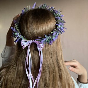 May include: A purple flower crown with a lavender ribbon tied in a bow. The crown is made of artificial flowers and is worn on a person's head.