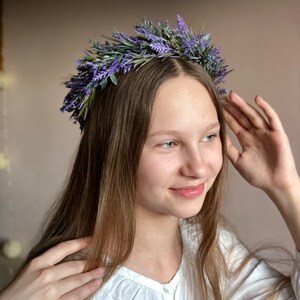 May include: A young person with long brown hair wearing a white shirt and a lavender flower crown.