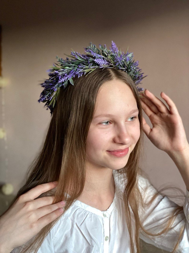 May include: A young person with long brown hair wearing a white shirt and a lavender flower crown.