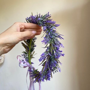May include: A purple flower crown with a lavender color scheme. The crown is made of artificial flowers and has a light purple ribbon tied around it.