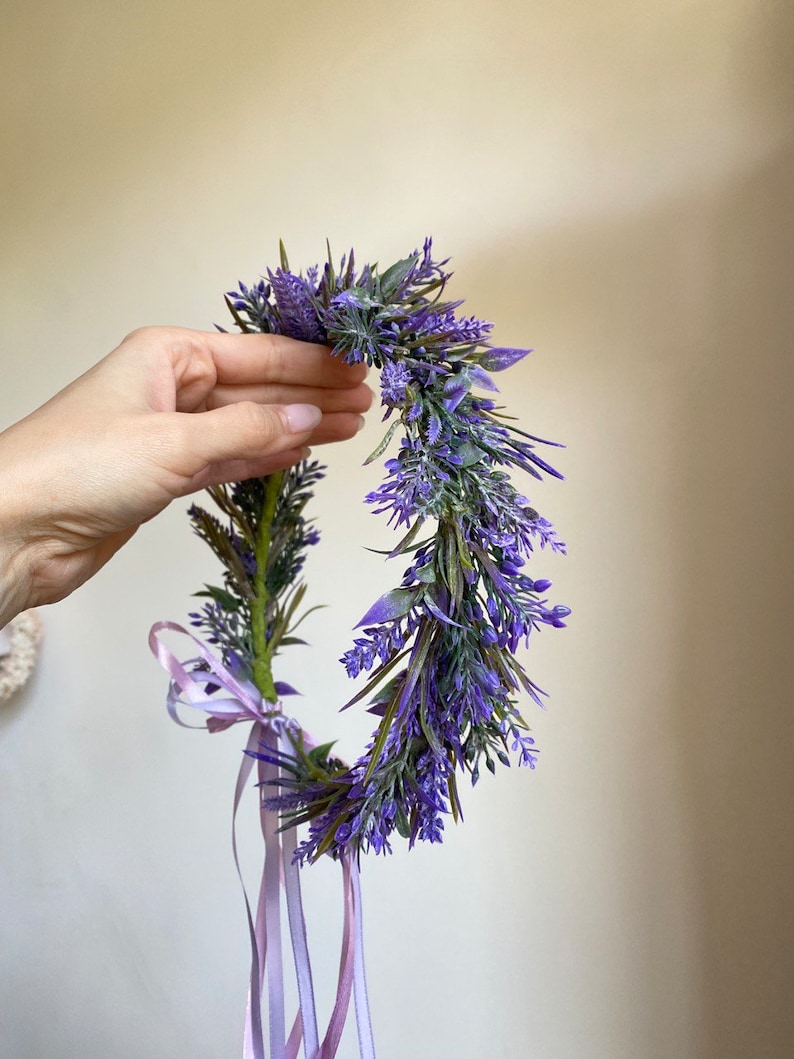 May include: A purple flower crown with a lavender color scheme. The crown is made of artificial flowers and has a light purple ribbon tied around it.