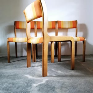 Op de afbeelding: Set van vier eetkamerstoelen in moderne stijl uit het midden van de eeuw met houten frames en oranje en gele gestreepte bekleding.