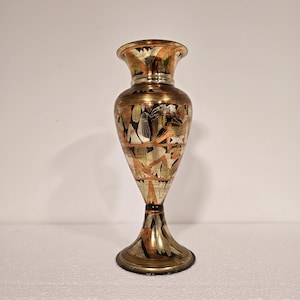 Könnte beinhalten: Eine kleine, dekorative Vase mit einer Kupfer- und Goldoberfläche. Die Vase hat ein geometrisches Muster und ist aus Metall.