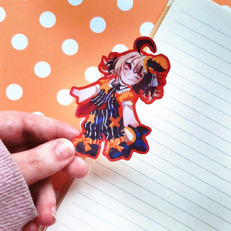 May include: A colorful anime-style character sticker with a black and white striped outfit, a yellow and orange top, and a black and orange hat. The sticker is on a white and orange polka dot background.