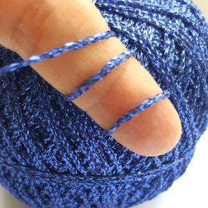 Può includere: Primo piano di un gomitolo di filo metallico blu. Il filo è avvolto attorno a un dito, mostrando la trama e la lucentezza del filo.