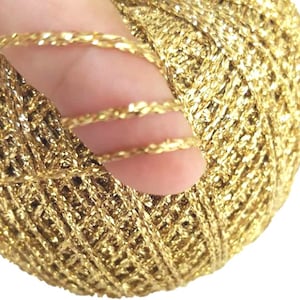 Può includere: Primo piano di un filo metallico dorato, che mostra la trama ritorta e intrecciata. Il filo è lucido e ha un riflesso metallico.