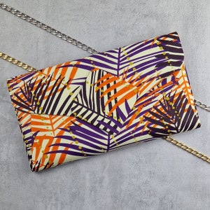 May include: A purple and orange clutch purse with a tropical leaf pattern. The clutch has a gold chain strap.
