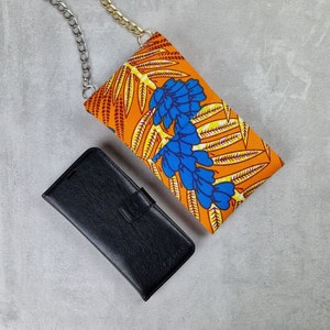 May include: A black leather phone case with a gold chain strap. The case is lying on a gray surface next to a colorful fabric phone case with a floral pattern in shades of orange, yellow, and blue.