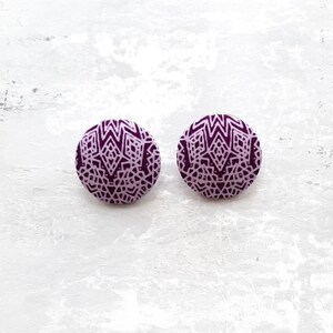 Puede incluir: Un par de pendientes redondos de botón con estampado morado y blanco.