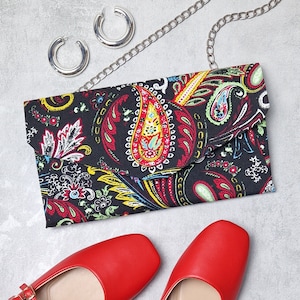 May include: A black clutch purse with a paisley pattern in red, yellow, and blue. The purse has a flap closure and a silver chain strap.