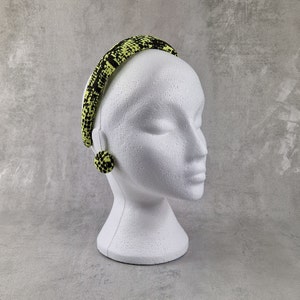 May include: A black and yellow patterned headband with a matching pair of earrings. The headband is on a white mannequin head.