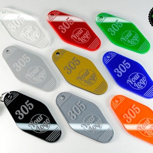 Puede incluir: Surtido de diez llaveros de motel en varios colores, incluyendo transparente, rojo, verde, dorado, plateado, negro, azul y naranja. Cada llavero presenta el número "305" y el texto "Your Logo" en una fuente blanca grabada.