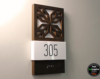 May include: A wooden room number sign with a decorative cutout design. The number 305 is displayed on a white plaque. The sign also includes braille lettering.