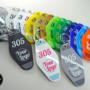 May include: A collection of retro-style keychains in various colors, including black, white, yellow, green, blue, orange, and red. Each keychain features the number "305" and the text "Your Logo". The keychains are attached to silver keyrings.