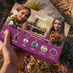 May include: A pink box with the words "moments KEEPSAKE DIY JEWELRY KIT" on the front. The box features a photo of two girls and a teddy bear. The box also shows examples of jewelry that can be made with the kit, including a necklace with a heart-shaped pendant, a necklace with a fabric pendant, and a ring with a turquoise stone.