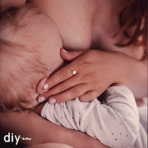 Könnte beinhalten: Nahaufnahme einer Mutter, die ein Baby stillt. Die Mutter trägt einen Ring mit einem runden, weißen Stein.