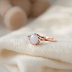 May include: A rose gold ring with a white oval-shaped gemstone.