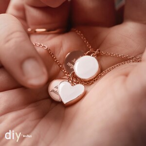 May include: Two gold necklaces with white enamel pendants. One pendant is a circle with the word "Never" partially visible. The other pendant is a heart with the word "in" partially visible.