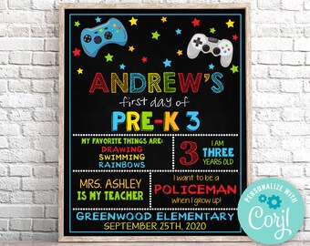 Könnte beinhalten: Ein schwarzes Schiefertafel-Schild mit einem farbenfrohen Design für den ersten Schultag eines Kindes. Das Schild lautet "Andrew's first day of Pre-K 3". Es enthält Details über die Lieblingsdinge des Kindes, sein Alter und seinen Lehrer. Das Schild enthält auch eine Grafik eines Videospiel-Controllers und Sterne.