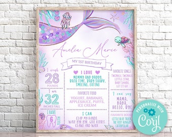 May include: A mermaid-themed first birthday sign with a purple and teal mermaid tail, a turtle, and a starfish. The sign includes the name "Amelia Marie", the child's age, weight, height, and number of teeth. It also lists favorite foods, songs, and activities.