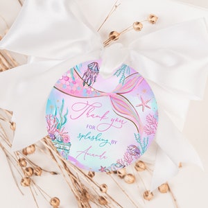 Op de afbeelding: Ronde roze en blauwe bedankkaart met een zeemeerminstaart, schelpen en de tekst "Bedankt voor het spetteren met Amanda".