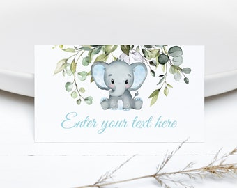 May include: A white card with a watercolor illustration of a gray elephant with blue ears sitting in a wreath of green leaves. The text "Enter your text here" is printed in blue cursive font.