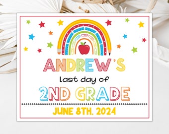 May include: A colorful sign for "Andrew's Last day of 2nd Grade" featuring a rainbow, apple, and stars. The text is in various colors, with the date "June 8th, 2024" at the bottom. The sign has a white background and a red border.
