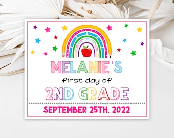 Puede incluir: Un letrero colorido con el texto "MELANIE'S first day of 2ND GRADE SEPTEMBER 25TH, 2022". Presenta un arcoíris, un lápiz, una manzana y estrellas. Ideal para una celebración de regreso a clases, el diseño es vibrante.
