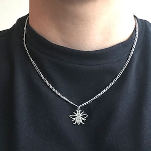 May include: A silver chain necklace with a bee pendant. The chain is a curb chain style.