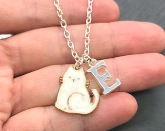 May include: A silver chain necklace with a white cat charm and a silver letter E charm.
